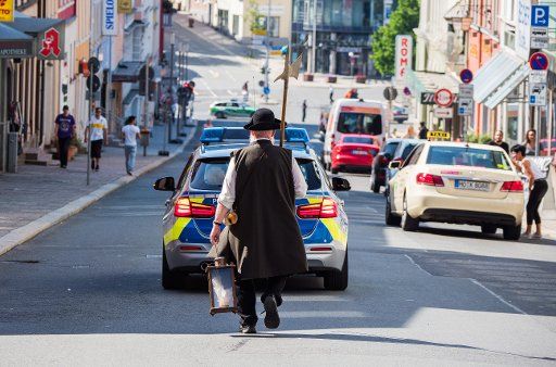 dpatop - 28 May 2018, Germany, Hof an der Saale: A man in historical dress follo0ws a police car in the procession of the 586th Schlappentag. The Schlappentag in Hof is one of Germany\