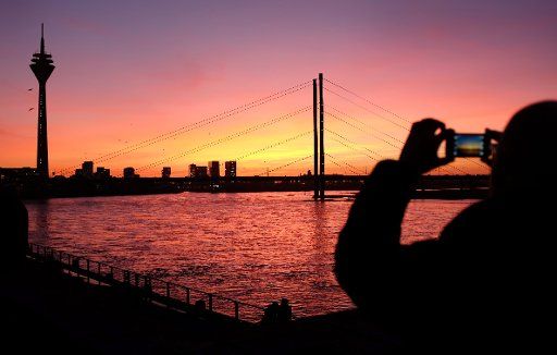 A passer-by takes a picture of the sunset at the Rhine in Duesseldorf, Germany, 02 December 2013. The setting sun colours the sky red and purple. Photo: Martin Gerten\/