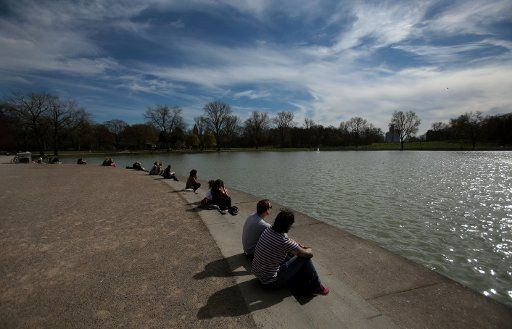 Pedestrian enjoy the warm spring weather as they sit on the embankment of a pond in Cologne, Germany, 20 March 2014. Photo: Oliver Berg\/