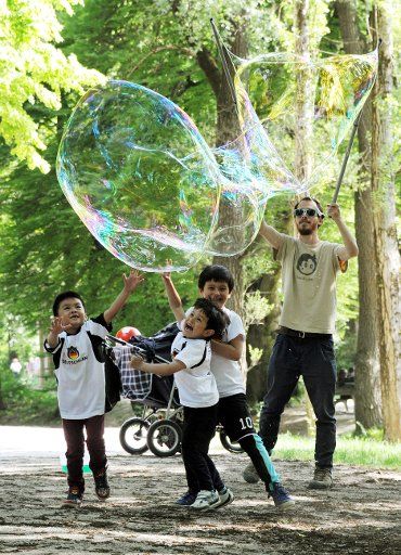 Children walk underneath a giant bubble in the English garden in Munich, Germany, 24 May 2014. Photo: Tobias Hase\/