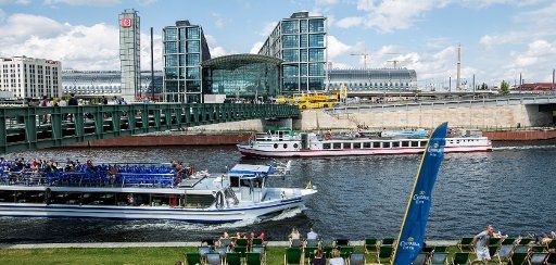 People sit at the banks of the Spree river opposite of the central station as two passenger ships pass by in Berlin, Germany, 25 July 2015. Photo: Lukas Schulze\/