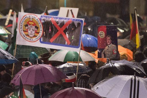 Pegida demonstrators hold signs lampooning Chancellor Merkel at Theaterplatz in Dresden, Germany, 30 November 2015. PHOTO: SEBASTIAN KAHNERT\/