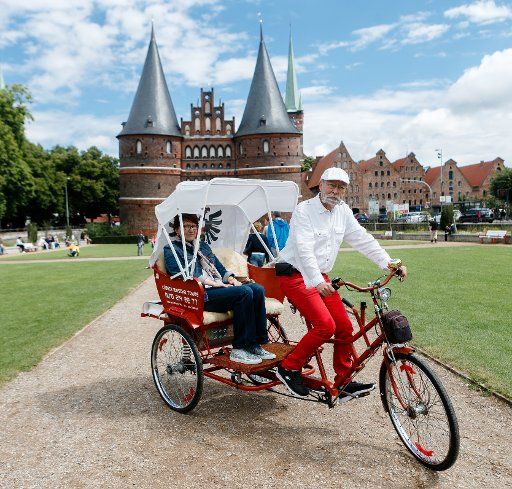 Hans-Heinrich Mangels takes a passenger for a drive past the Holsten Gate with his cycle rickshaw in Luebeck, Germany, 1 August 2016. Photo: Markus Scholz\/