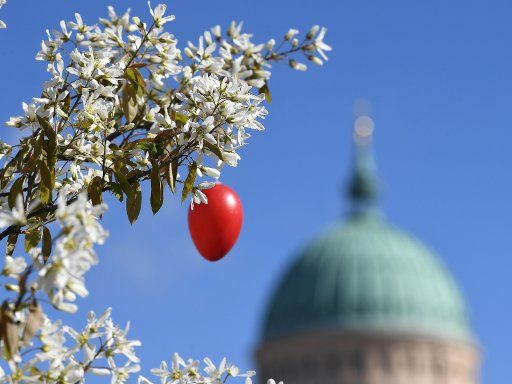 A red Easter egg hangs from a bush in front of St. Nicholas\