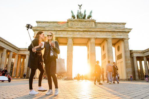 Two tourists photograph themselves in the orange light of sunset in front of the Brandenburger Gate in Berlin, Germany, 28 March 2017. Photo: Gregor Fischer\/