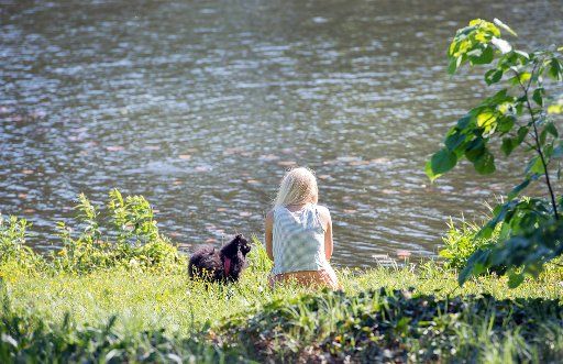 A woman enjoys the sunny weather with a dog in the park of Charlottenburg Palace in Berlin, Germany, 18 May 2017. Photo: Paul Zinken\/