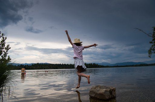 Seven year old Ann-Louise jumps into the water from a stone at the Kirchsee lake while dark clouds veil the sky at the horizon in Sachsenkam, Germany, 21 July 2017. Photo: Peter Kneffel\/