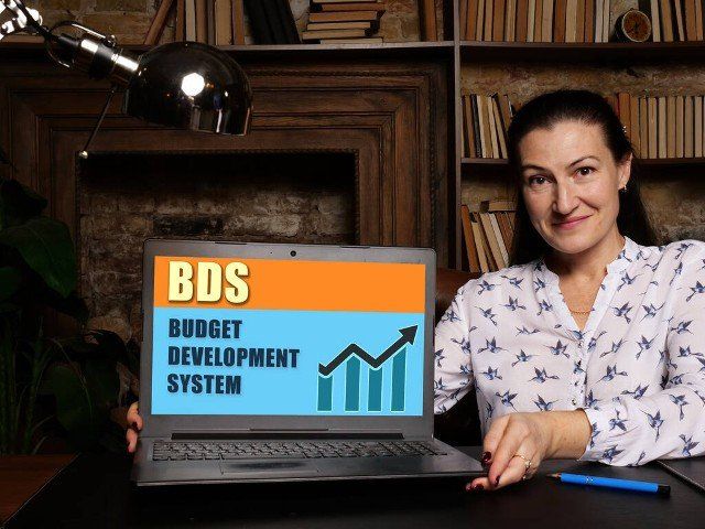 Woman showing laptop computer with  BDS BUDGET DEVELOPMENT SYSTEM icon on screen background, success in business concep