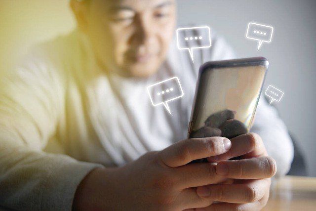 Asian man sending text message and sms with smartphone. Guy texting and using mobile phone late at night in dark. Communication or sexting concept. Chat icons. with selective focus on phone