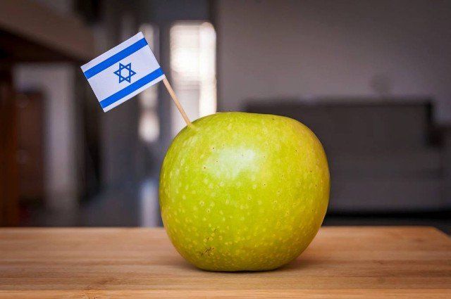 Green Granny Smith apple with a tiny flag of Israel on a wooden table. A concept image for the Jewish New Year Rosh Hashana or Made in Israel, anti BDS movement, Israeli agricultural fruit product.