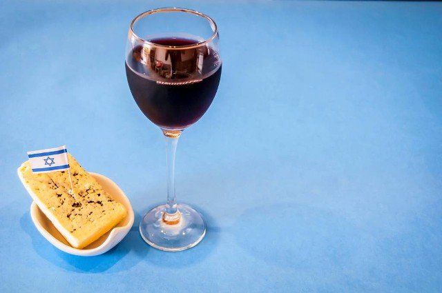 A glass of red wine with a piece of blue cheese on a small plate with a tiny flag of Israel on a light blue background. Israeli wines concept, Made in Israel. Israeli products