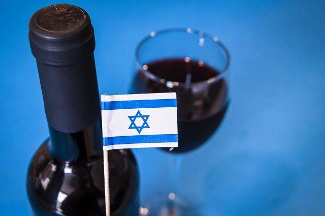 Flag of Israel with a wine bottle and a glass of red wine in the background. Israeli wines concept, Made in Israel. Israeli products vs. BDS political campaign.