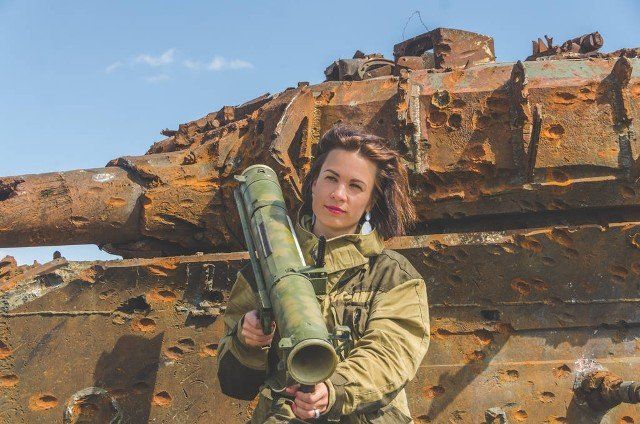 Sunny day girl in uniform with a Bazooka on the background of a broken tank on the battlefield