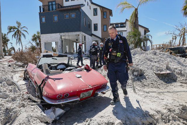 An Urban Search and Rescue Florida Task Force 2 team member walks past a 1965 Corvette damaged by flood waters caused by Hurricane Ian on Fort Myers Beach on Monday, October 3, 2022. (Al Diaz\/Miami Herald\/TNS