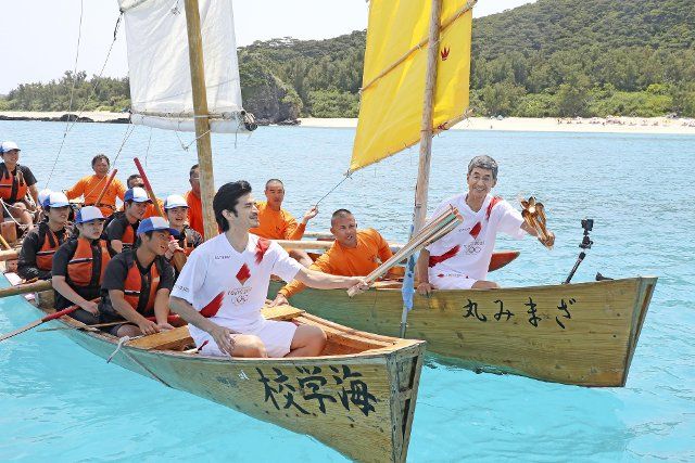 The Tokyo Olympic flame is passed from torch to torch by relay participants on traditional rowboats on May 2, 2021, off Zamami in Japan\