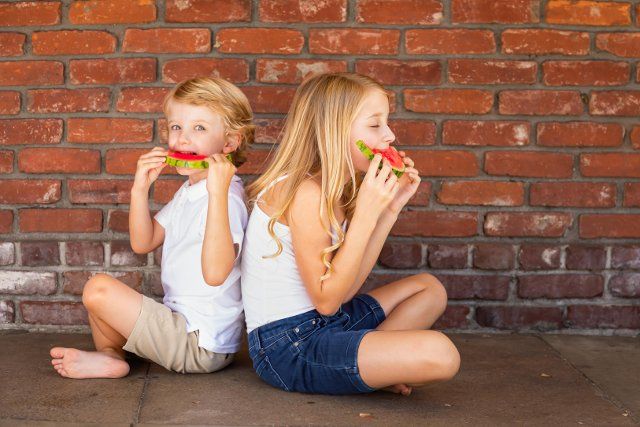 Cute young cuacasian boy and girl eating watermelon against brick