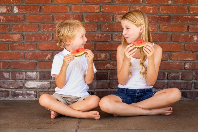 Cute young cuacasian boy and girl eating watermelon against brick