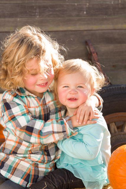 Sweet little boy plays with his baby sister in a rustic ranch setting at the pumpkin