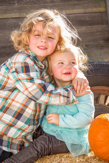 Sweet little boy plays with his baby sister in a rustic ranch setting at the pumpkin