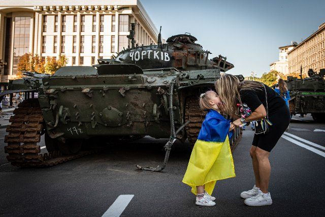 A little girl Sophia kisses her mother as she ties a Ukrainian flag to her daughter in front of the demolished Russian tank showcased in Kyiv. Amid the Independence Day of Ukraine, and nearly 6 months after the full-scale invasion of Ukraine on February 24, the country\