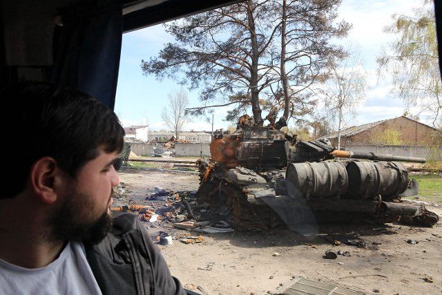 A man travelling in a bus looks at a destroyed Russian military vehicle marked with Russia\