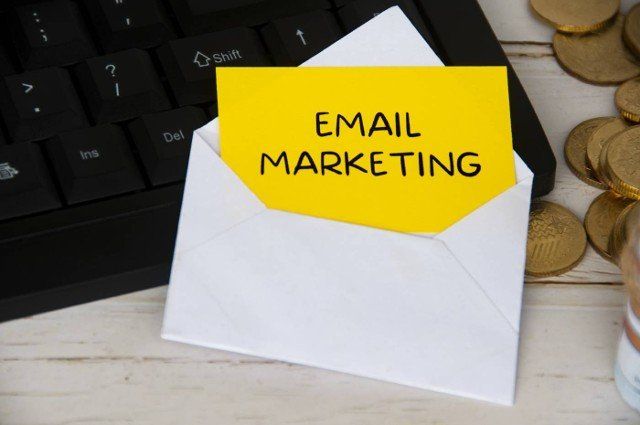 Email marketing text on yellow notepad in an envelope on keyboard computer with gold coins. Online business concept