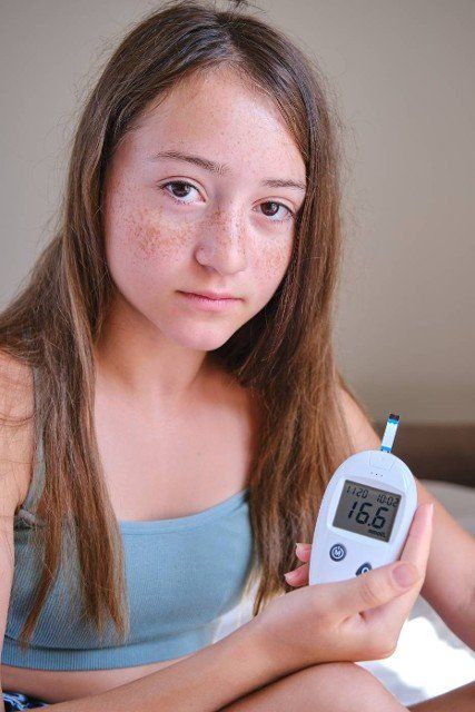 A teenage girl shows the screen of a glucometer with the results of a blood test for diabetes into the camera. Lifestyle of a child with diabetes.