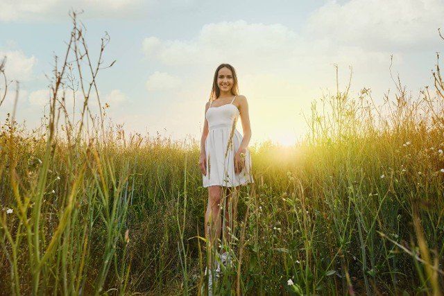 Beautiful young woman in white dress walking in the field over the sunset