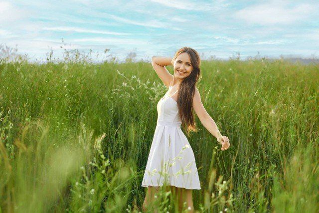 Smiling young woman in white sundress feeling free in the field