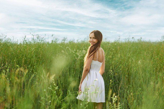 Joyful young woman in white short dress in the field turning back and looking over the shoulder