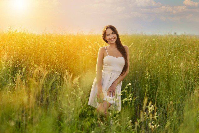 Beautiful young woman in white tank top and skirt dancing in the field under vibrant sunset
