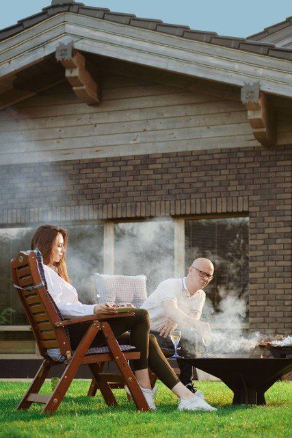 Happy couple barbecuing outdoors. Man turning sausages on grill.