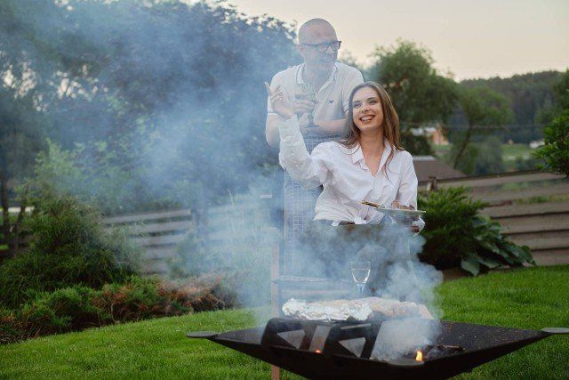 Happy couple making barbecue on backyard in the evening
