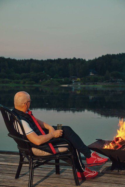 Bald man rests in the evening sitting on the pier by the fire