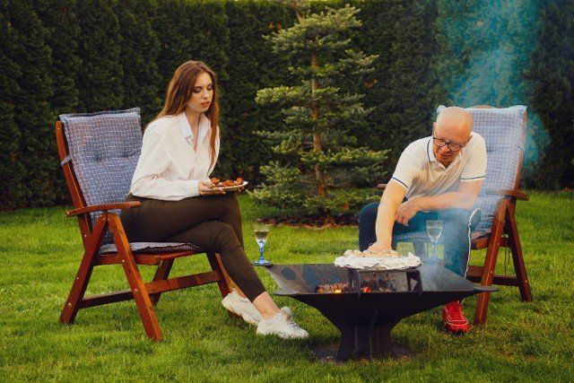 Couple making meat and vegetables on grill in backyard