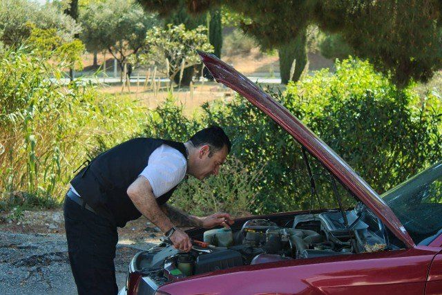 mature man fixing a breakdown in his car engine with tools on the side of the road