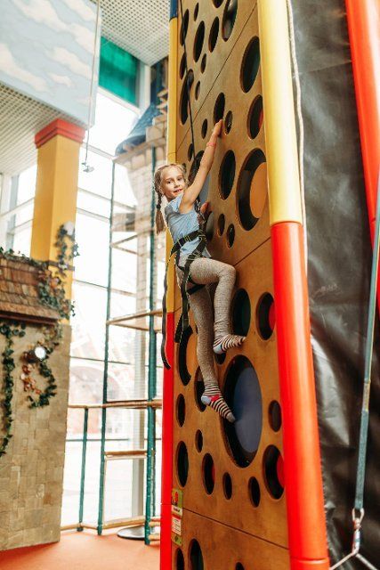 Funny girl climbing walls in children game center. Excited child having fun on playground indoors. Female kid playing in amusement centre,  activity attraction