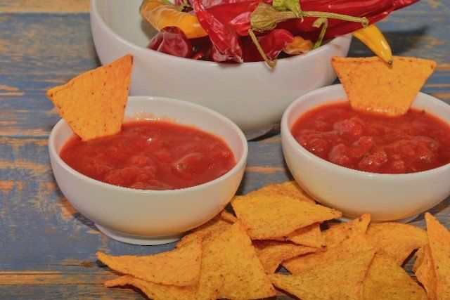Chili corn-chips with salsa dip and chili peppers on wooden background.