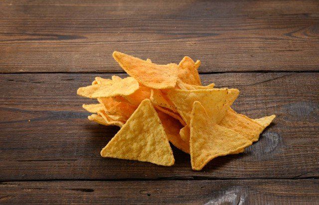 pile of corn tortilla chips or nachos on a brown wooden background,  close up
