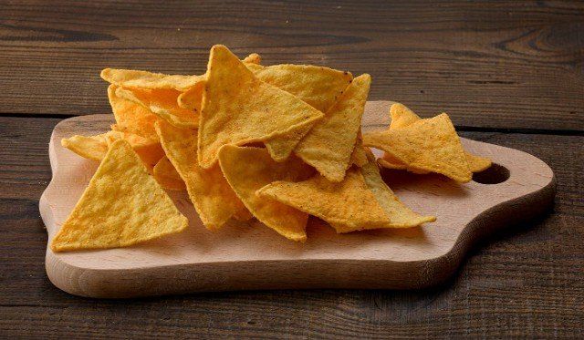 pile of corn tortilla chips or nachos on a brown wooden background,  close up