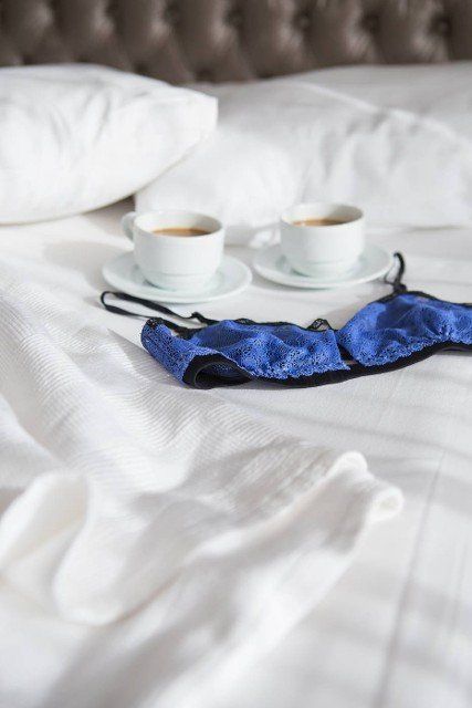 two cups of coffee and a beautiful bra on a white bed,  close-up