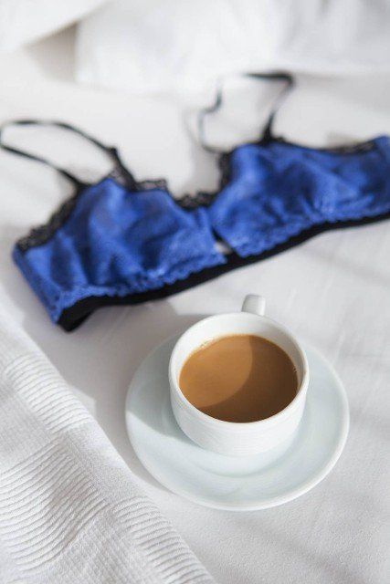 cup of coffee and a beautiful bra on a white bed