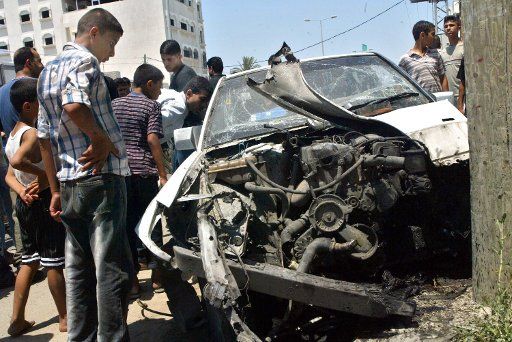 Palestinian civilians and police officers inspect the wreckage of a car in Gaza City on July 7 2004 after an explosion ripped through its engine. Palestinian officias said it was caused by an Israeli missile strike which wounded three people....