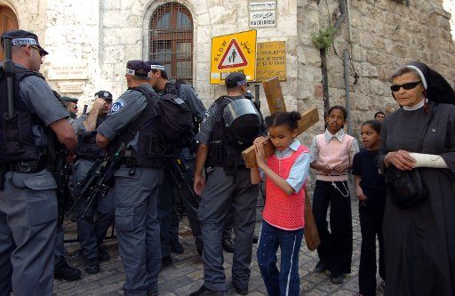 A child carries a cross on Good Friday  past Israeli border police on the Via Dolorosa the traditionally believed  route where Jesus carried his cross before being crucified in the Old City of Jerusalem Israel on April 14 2006. (UPI Photo\/Debbie Hill)