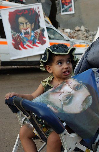 A young boy in a stroller holds a poster of Hezbollah leader Hassan Nasrallah in front of a painting showing U.S. Secretary of Sate Condoleezza Rice with fangs in Beirut\