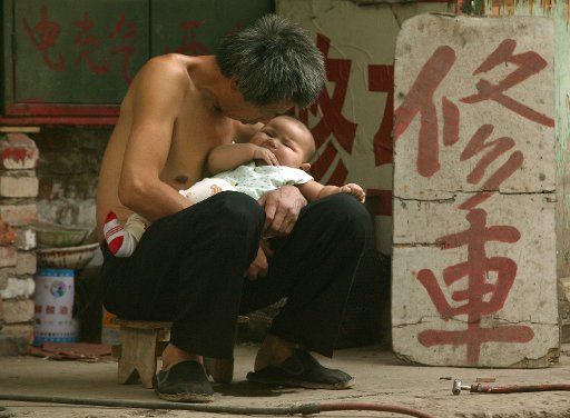 A father holds his very young son while waiting for customers at his sidewalk bicycle repair shop in downtown Beijing September 22 2006.  The population of China rose to 1.265 billion people by the end of 2000 an increase of 11.6 percent from 1990...