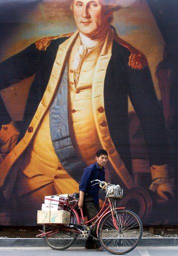 A Chinese delivery man unlocks his bike in front a a giant housing billboard featuring the first U.S President George Washington in downtown Beijing China on July 03 2007. Many Chinese companies from real estate to investment firms frequently ...