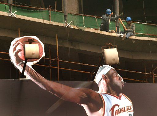 Chinese laborers work on construction site behind a massive Nike China billboard featuring NBA stars to promote the company\