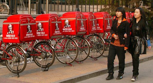 Chinese woman walk past new KFC delivery mopeds and bicycles parked outside one of its stores in downtown Beijing April 4 2009. As China continues to open up to Western culture at breakneck speed American businesses are starting to see major ...
