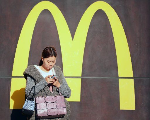 A Chinese woman stands in the sun in front of a McDonald\